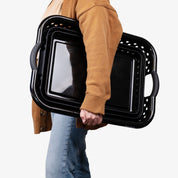 Person holding folded collapsible plastic laundry basket with handles on a white background