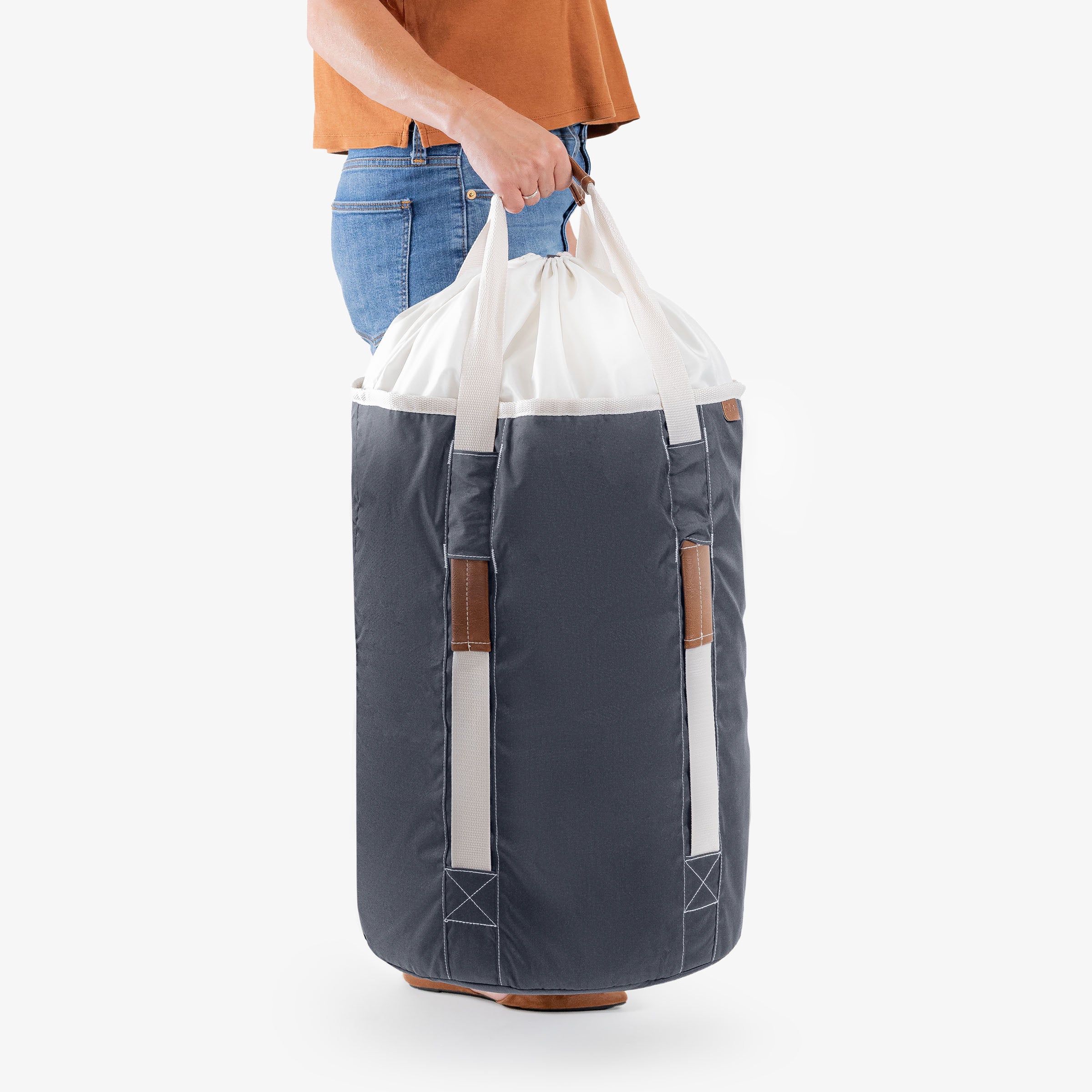 Person holding a large gray laundry backpack duffel bag with a white drawstring bag over it on a white background