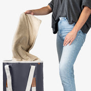 Person holding a beige towel above a charcoal laundry backpack duffel bag 
on a white background