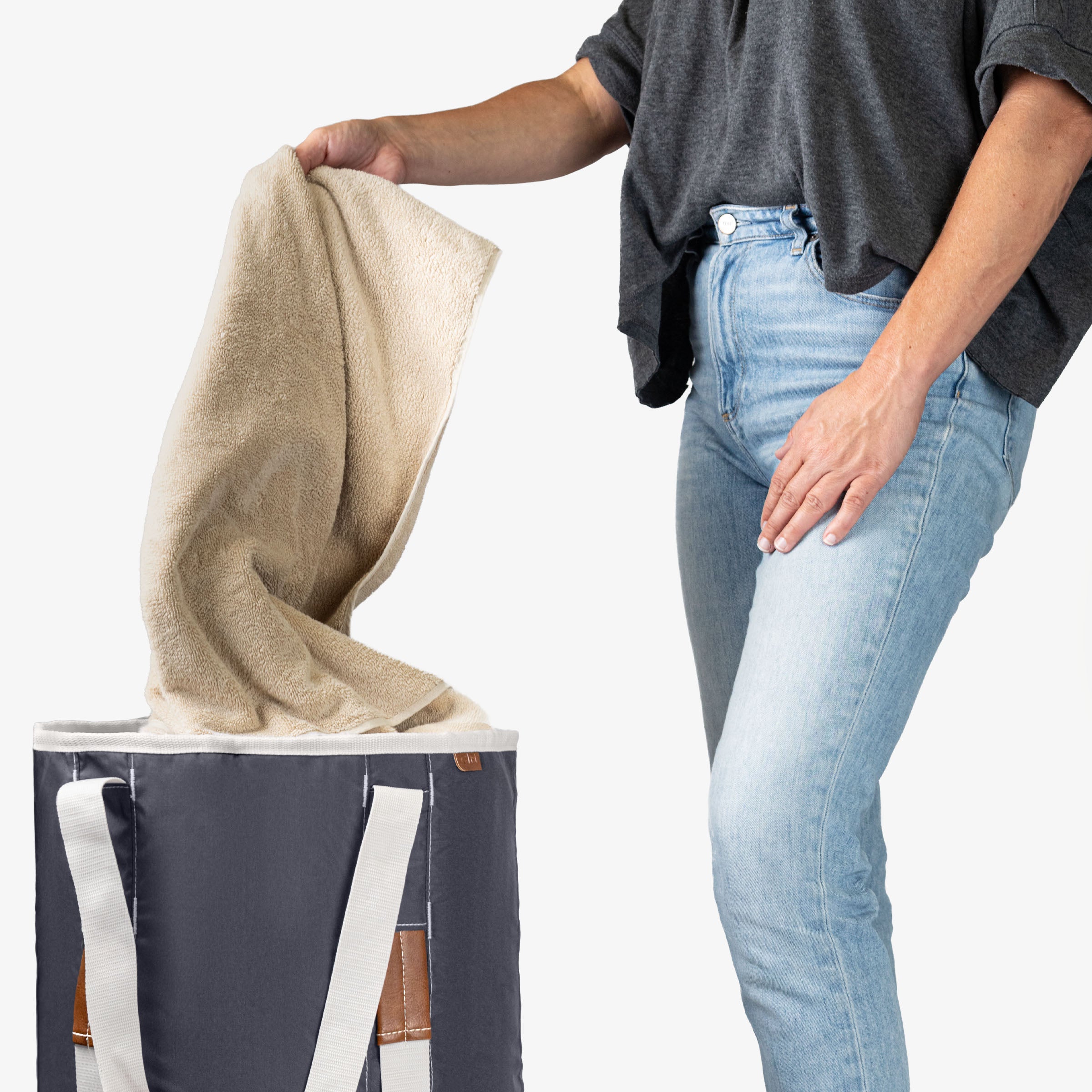 Person holding a beige towel above a charcoal laundry backpack duffel bag 
on a white background