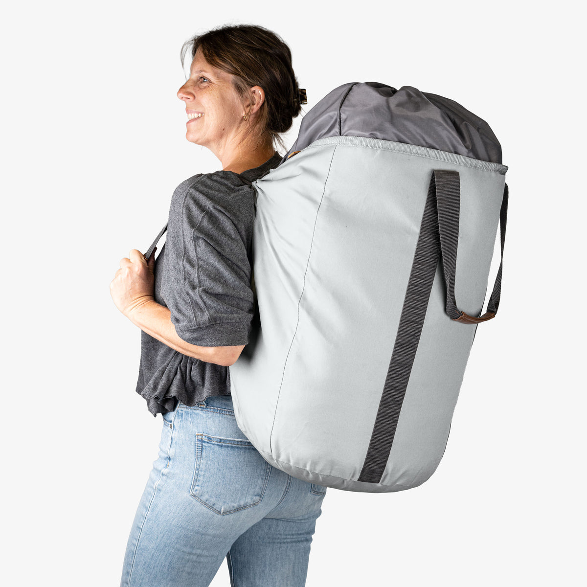 Person wearing a large gray laundry backpack duffel bag with a white top on a white background