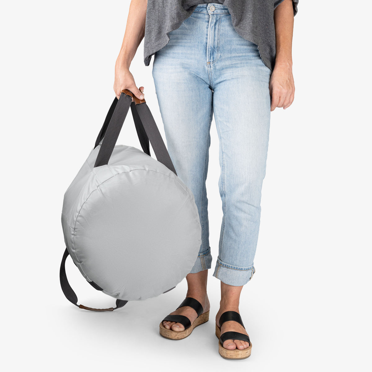 Person holding a gray round laundry backpack duffel bag with a white background