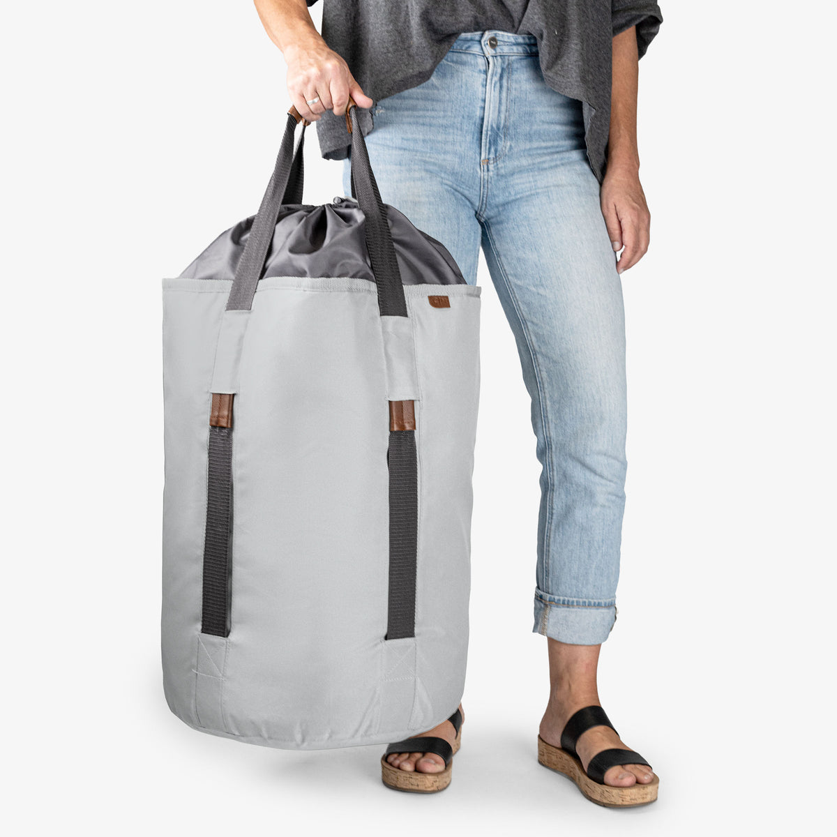 Person holding a large gray and black laundry backpack duffel bag on a white background