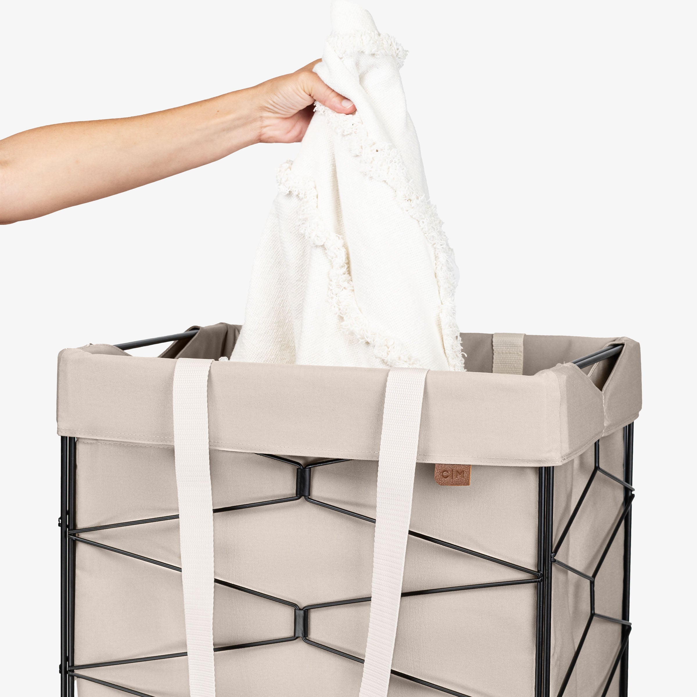 Person placing a white towel into a cream laundry basket on a white background