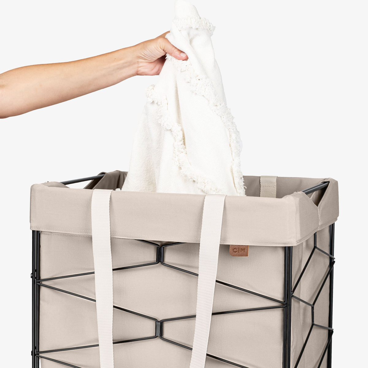 Person placing a white towel into a cream laundry basket on a white background