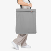 Person holding a gray tote bag on a white background