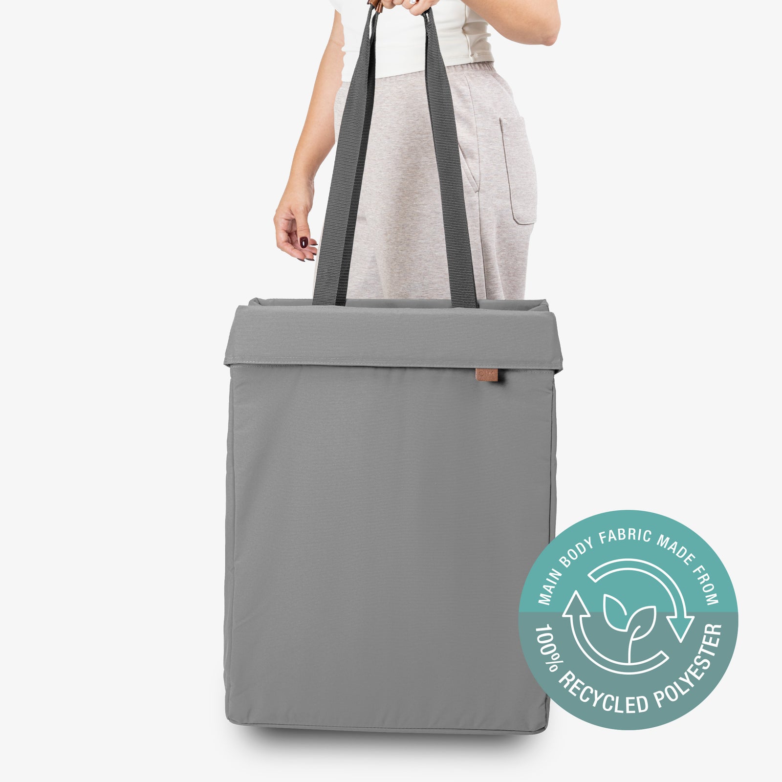 Gray tote bag with recycled polyester label held by a person on a white background