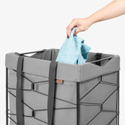 Person placing a blue towel into a gray laundry basket on a white background
