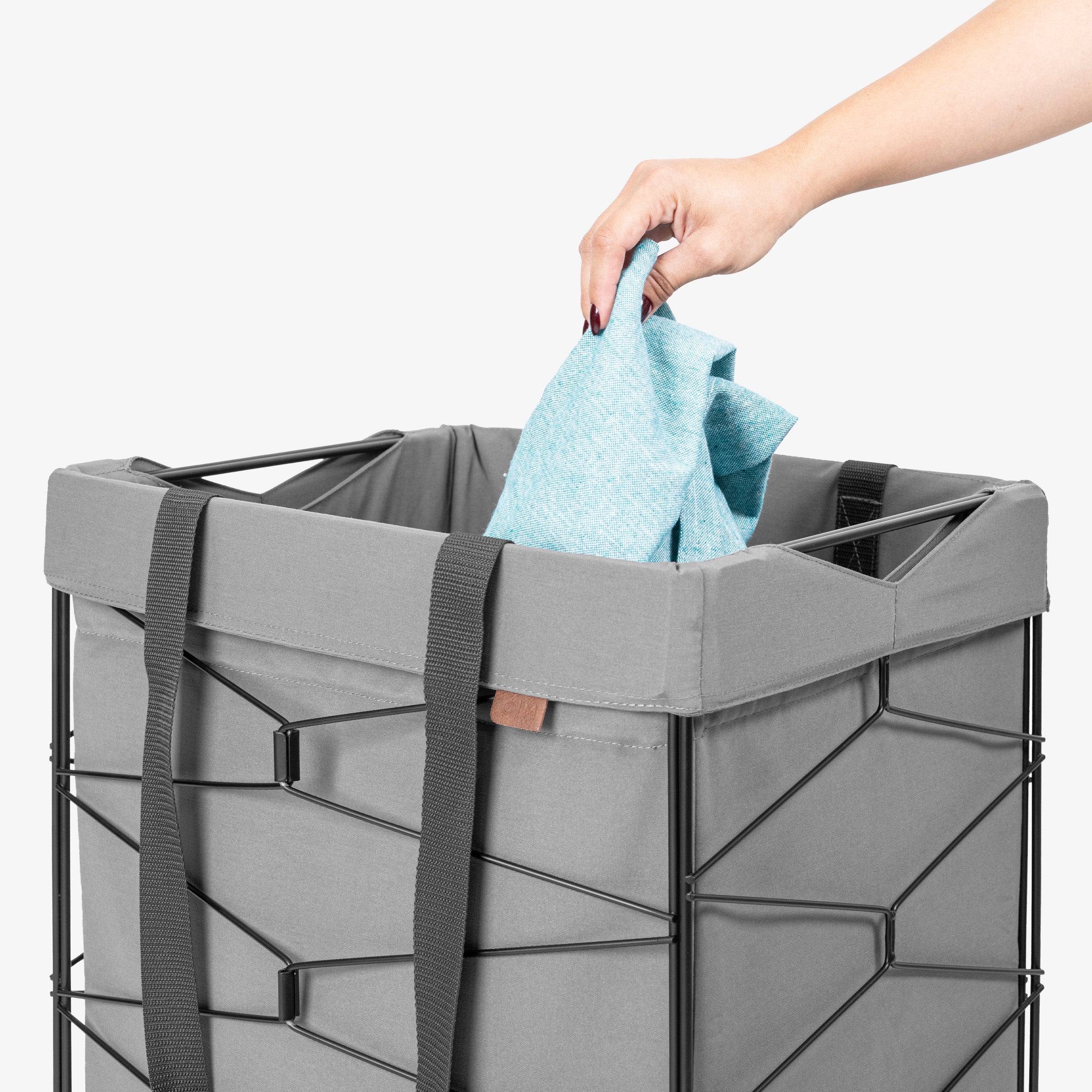 Person placing a blue towel into a gray laundry basket on a white background