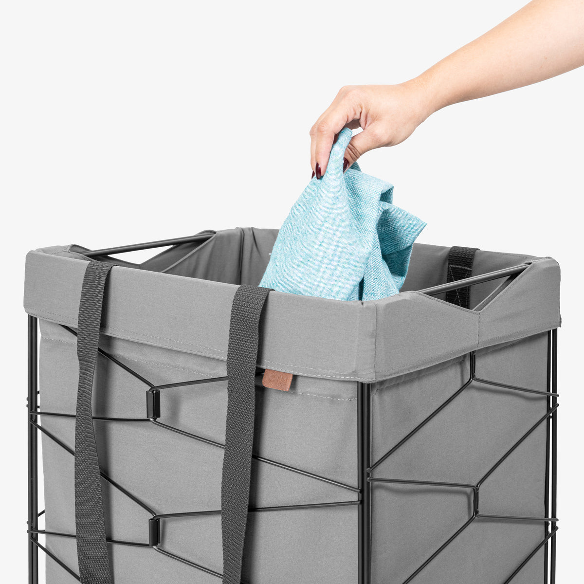 Person placing a blue towel into a gray laundry basket on a white background