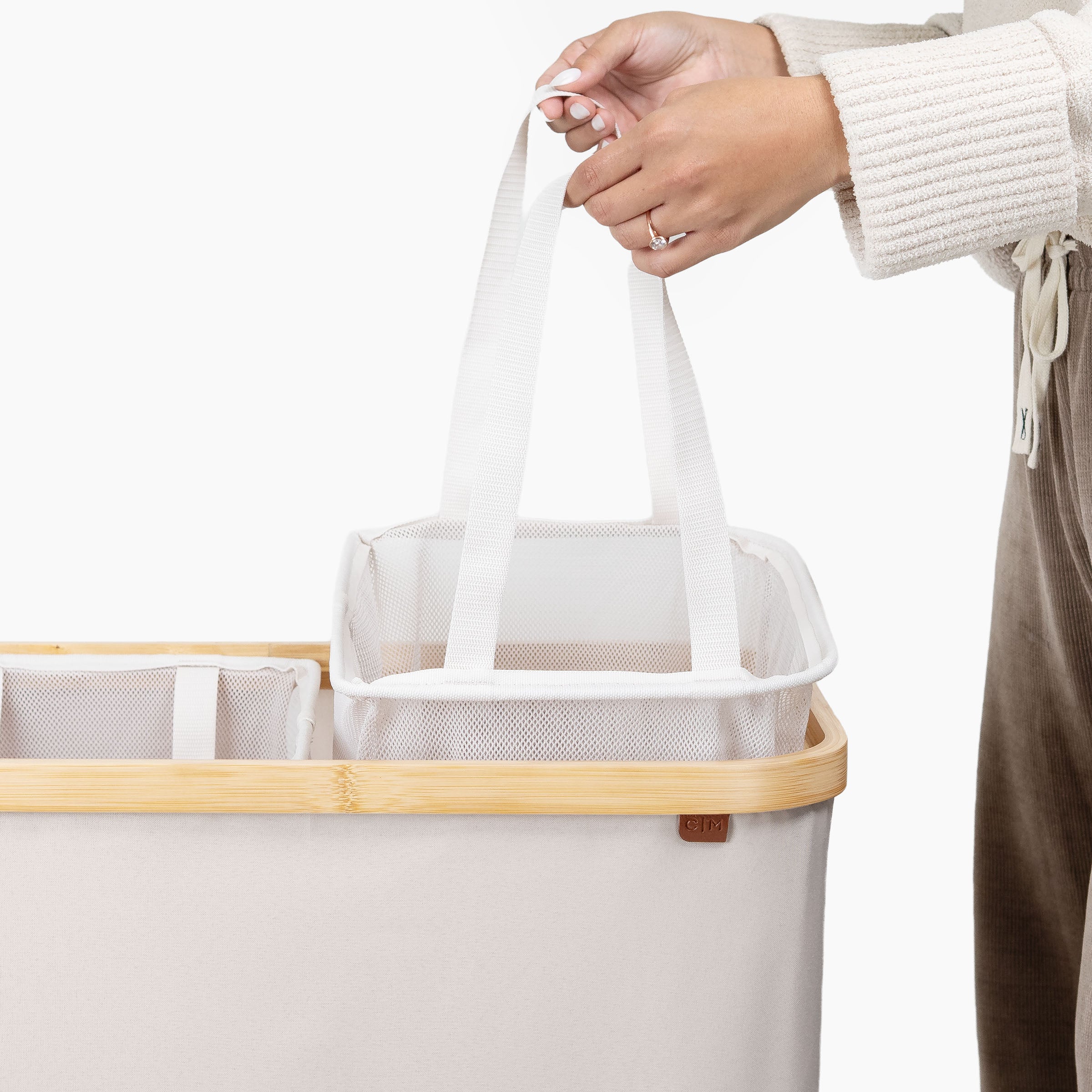 Person holding a white mesh bag over a beige laundry basket with wooden handle.
