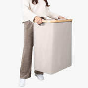 Person holding a beige laundry basket with a wooden handle on a white background