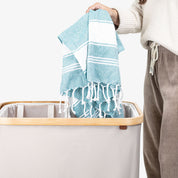 Person holding a blue towel above a laundry basket with a white background