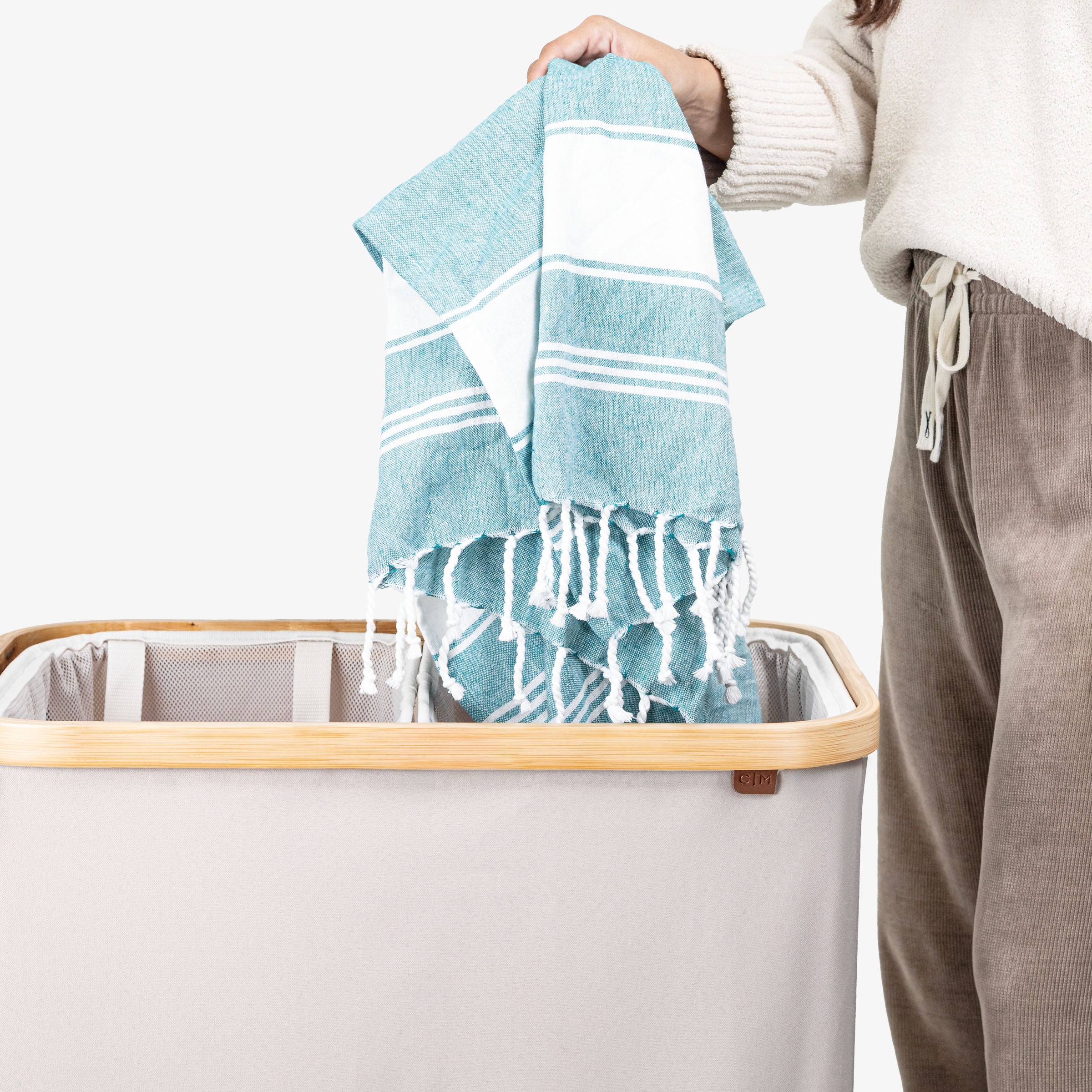 Person holding a blue towel above a laundry basket with a white background