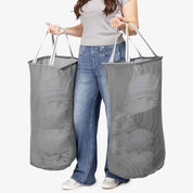 Person holding two large gray laundry bags against a white background