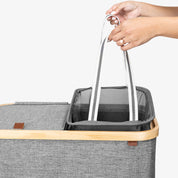 Gray lidded laundry hamper with wooden handle held by a hand on a white background