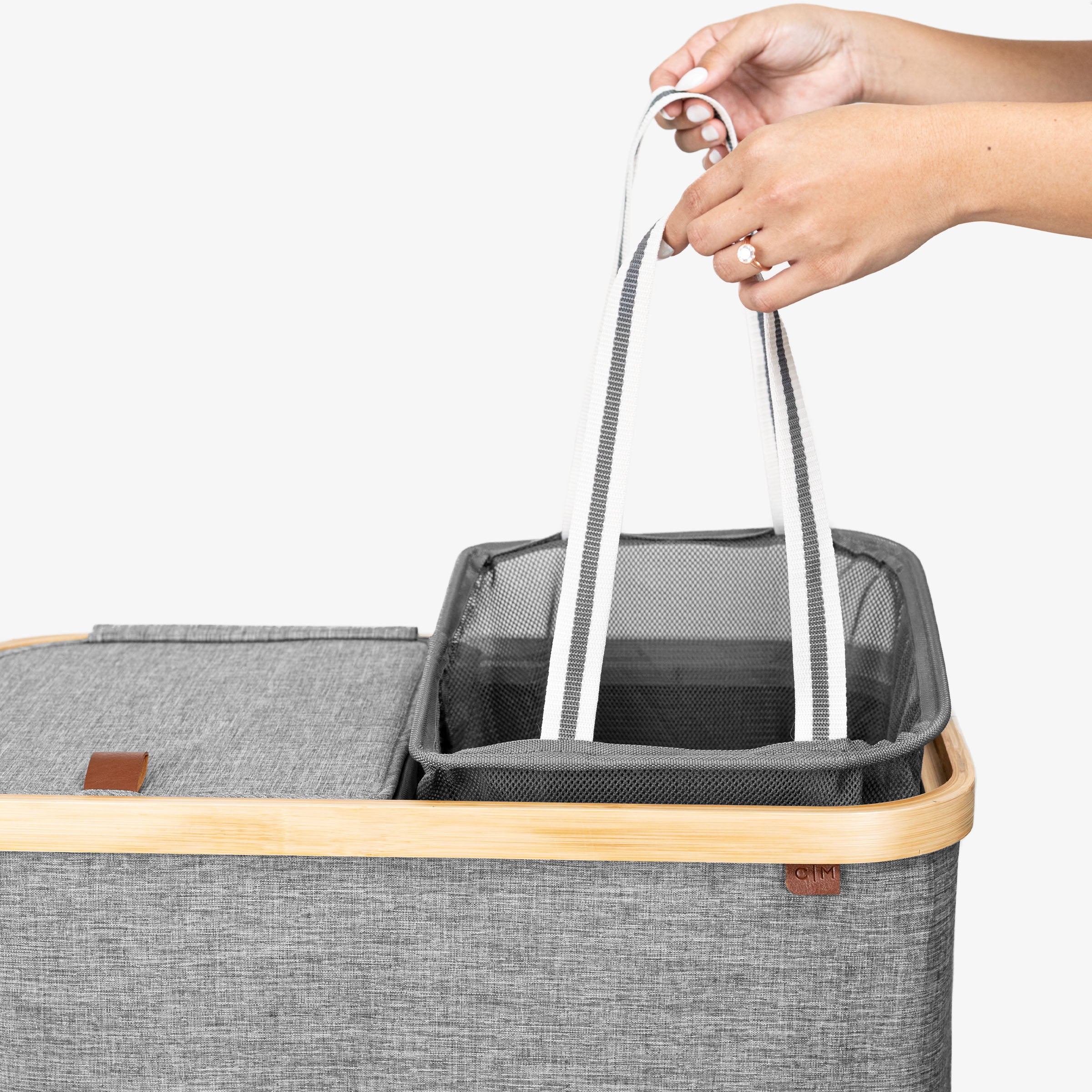 Gray lidded laundry hamper with wooden handle held by a hand on a white background