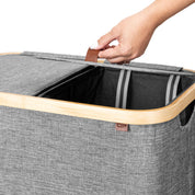 Gray laundry basket with wooden handle and visible brand logo, hand lifting lid.