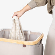 Person placing a knitted item into a laundry basket with a neutral background