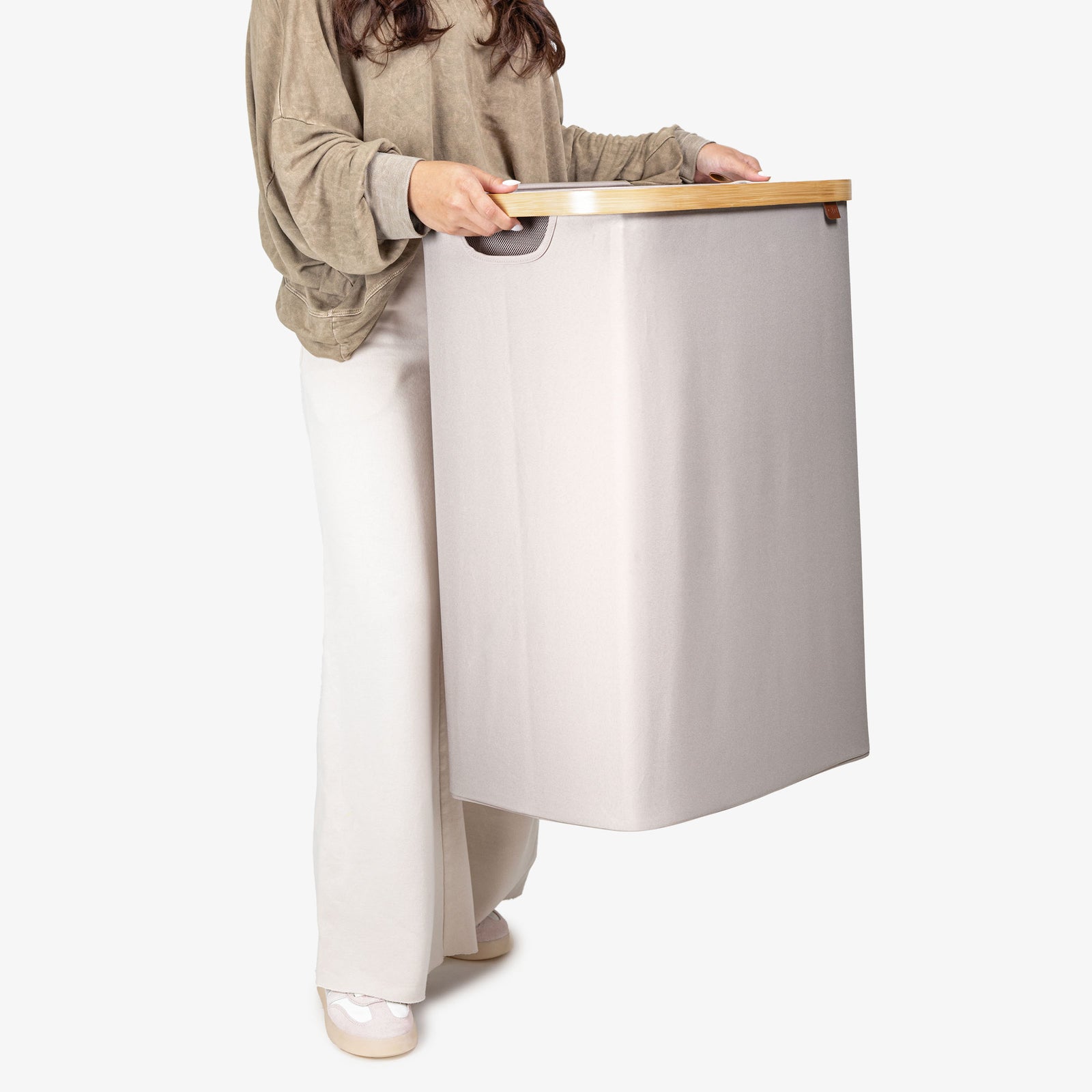Person holding a modern, light-colored lidded hamper with a wooden accent on a white background