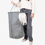 Person holding a large gray laundry basket with a white towel draped over it against a white background