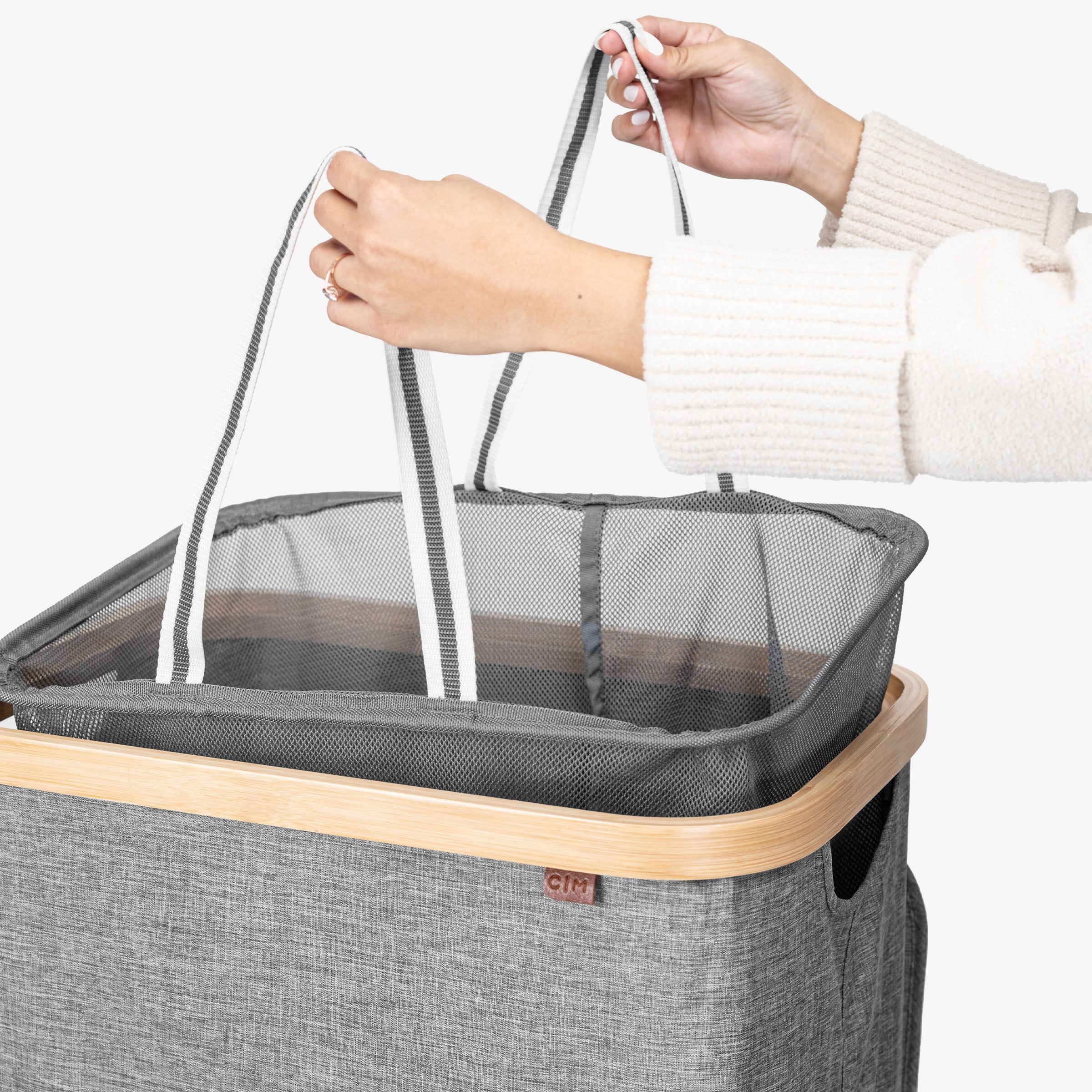 Person lifting a gray laundry basket with a mesh compartment and wooden rim.