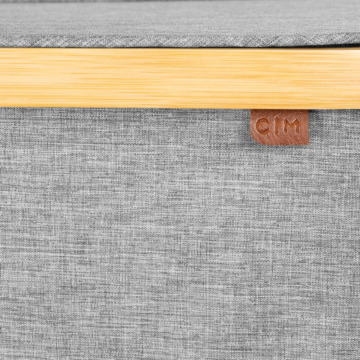 Close-up of a gray textured surface with a wooden edge and a brown leather patch with 'C|M' branding.