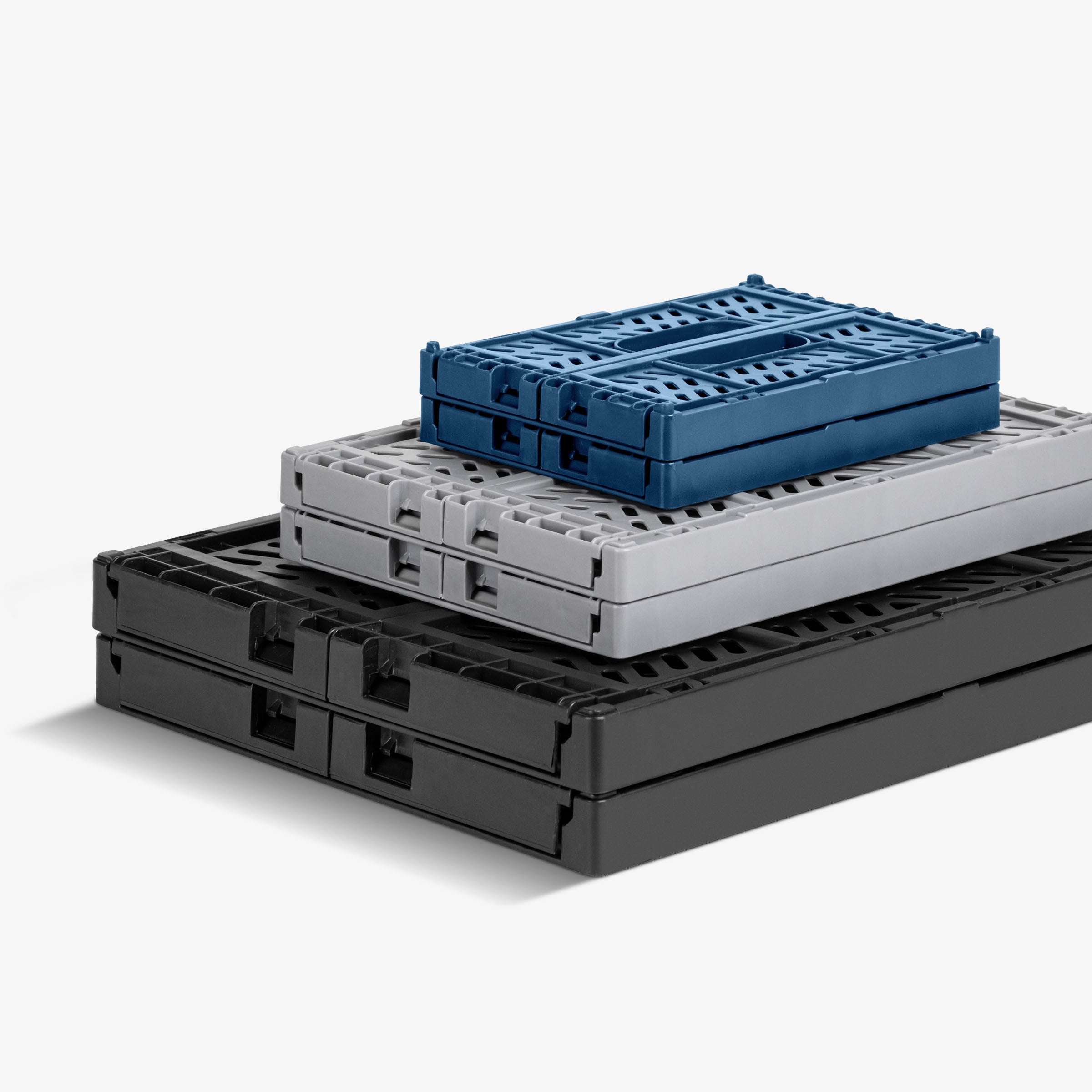 Stack of folded gray, black, and blue mini collapsible storage crates on a white background