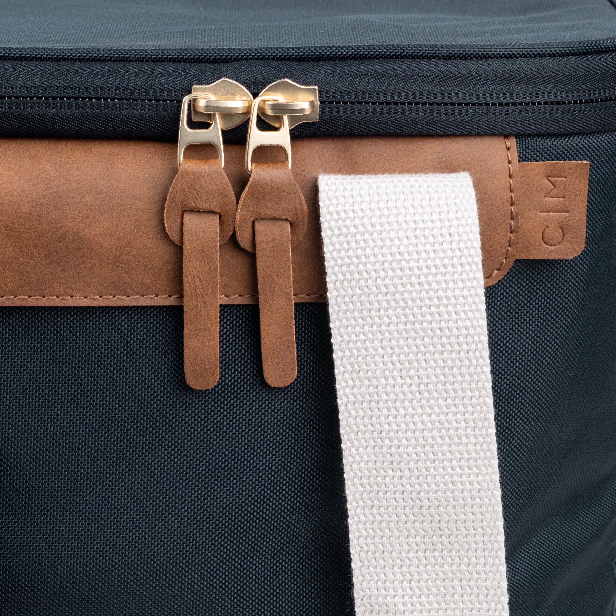Close up of Malibu collapsible cooler bag with navy blue body, brown leather accents, and white straps with brand label C|M
