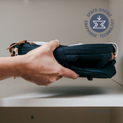 Hand holding a folded dark blue collapsible cooler with 'Space-Saving Snap hinge Technology' logo in the corner.