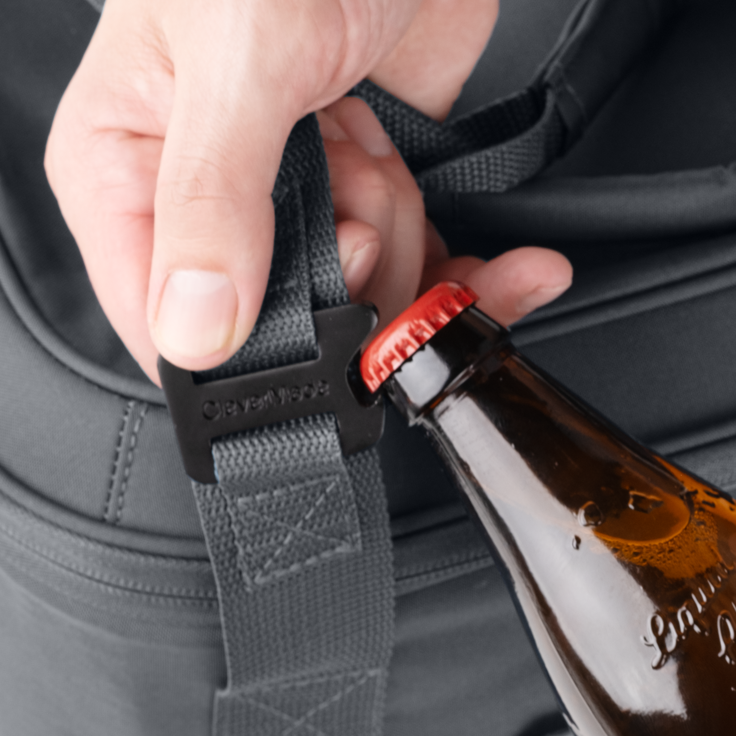 Person using a bottle opener attached to a bag strap with a beer bottle.