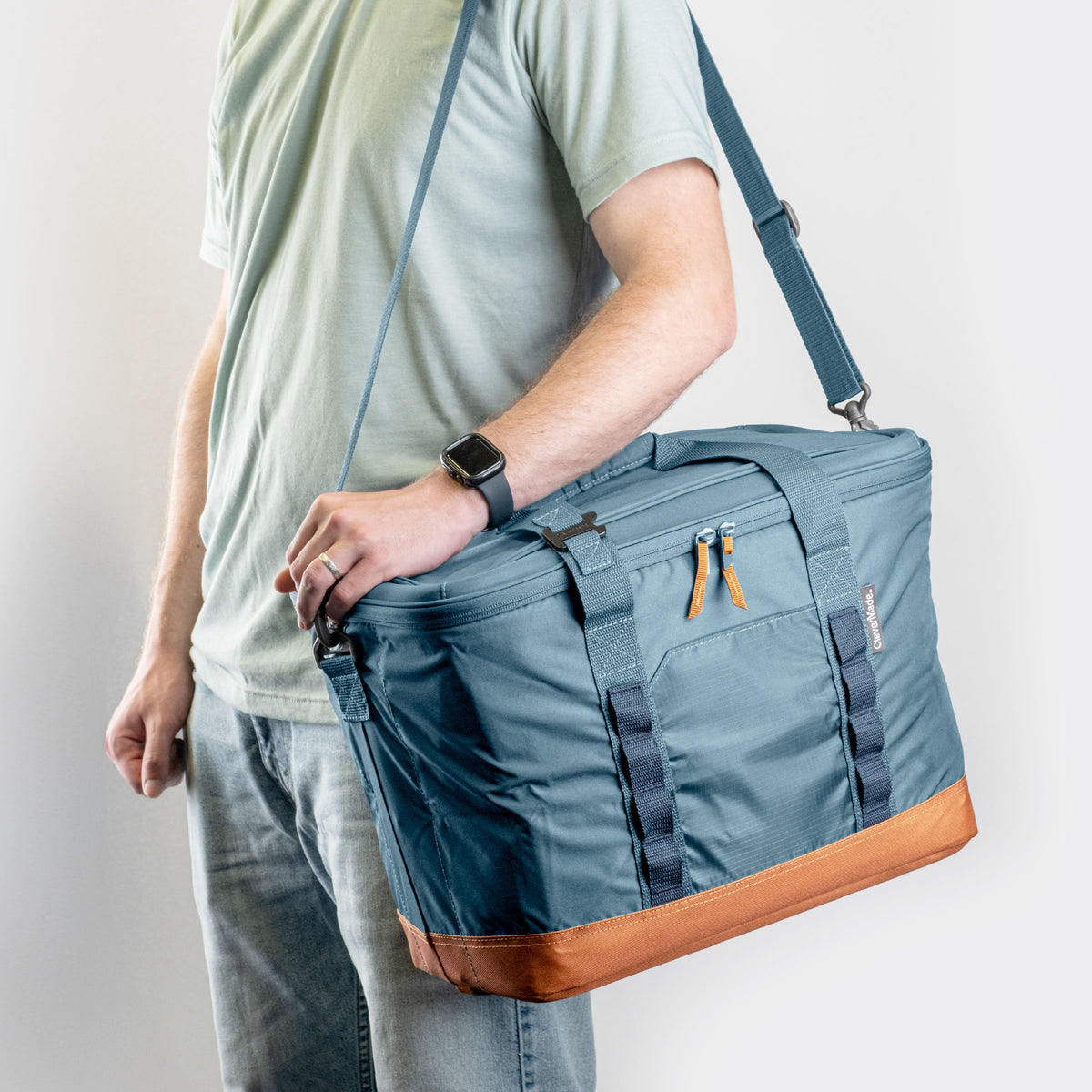 Person carrying a blue cooler bag with brown bottom section on a plain background