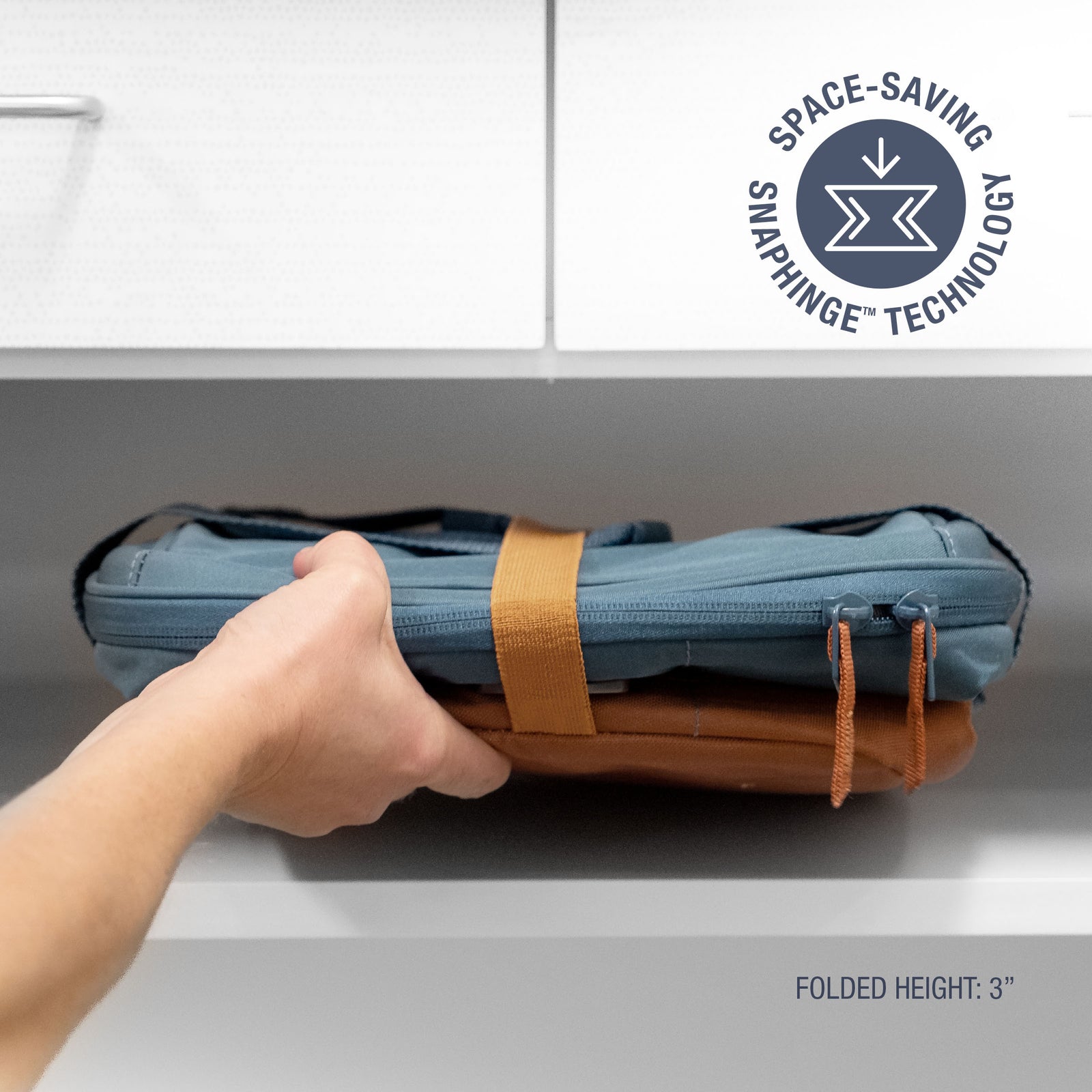 Hand holding a folded blue and brown bag with 'Space-Saving Snap hinge Technology' label.