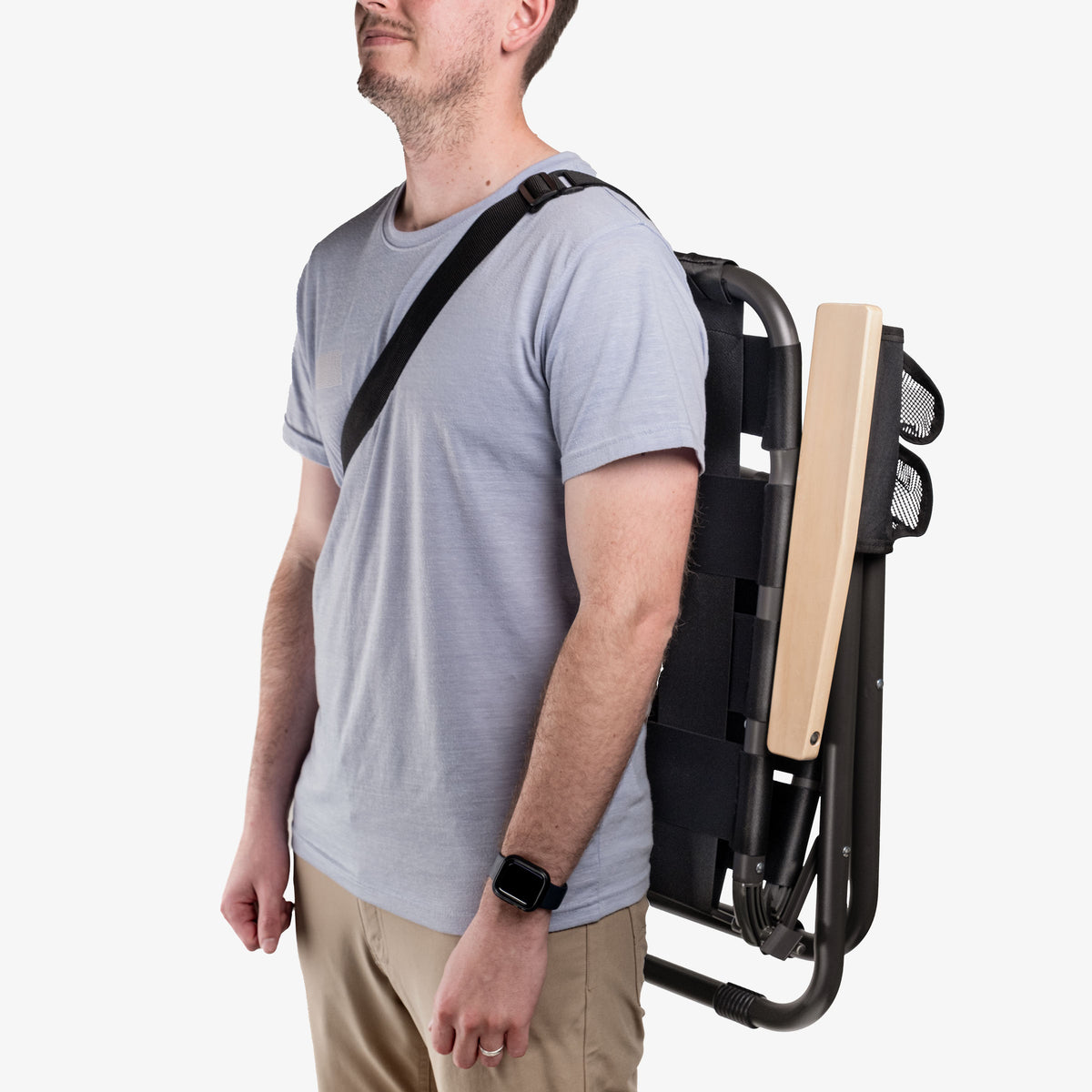 Person carrying folded black Kove outdoor chair with strap over shoulder 