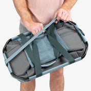 Person holding a gray duffel bag with green straps on a white background