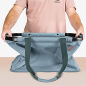 Person holding a large blue bag with a visible brand logo on a neutral background