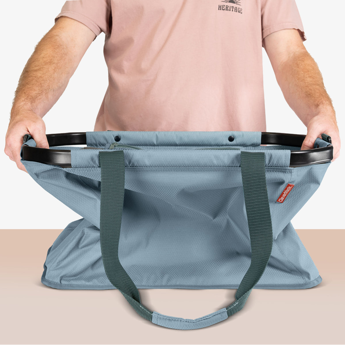 Person holding a large blue bag with a visible brand logo on a neutral background