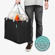Person holding a black tote bag with sports equipment, featuring a label indicating 100% recycled polyester.