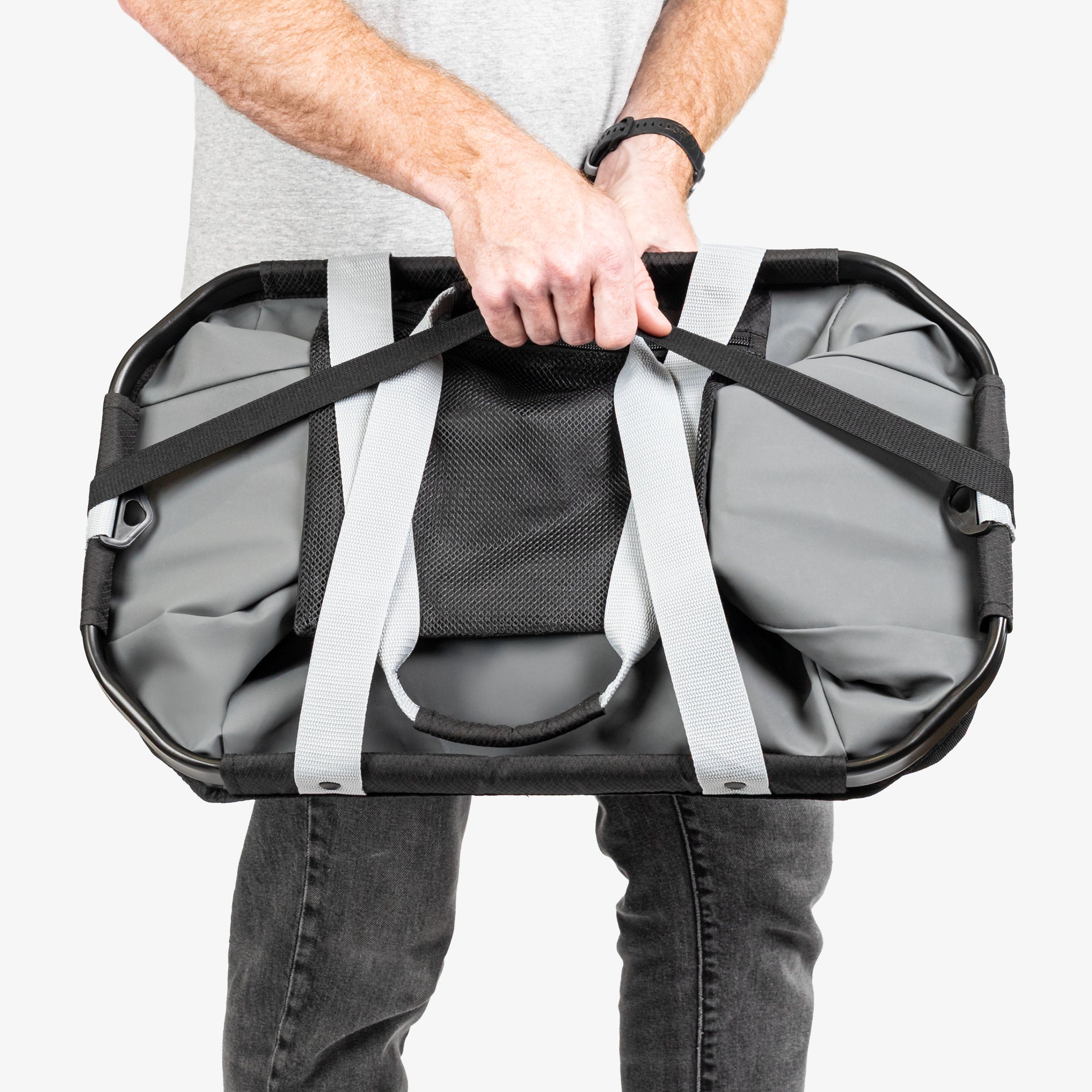 Person holding a large gray duffel bag with straps on a white background