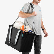 Person carrying a black sports bag filled with soccer balls and equipment on a white background
