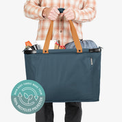 Person holding a blue tote bag with brown handles, featuring a recycling logo on a white background.