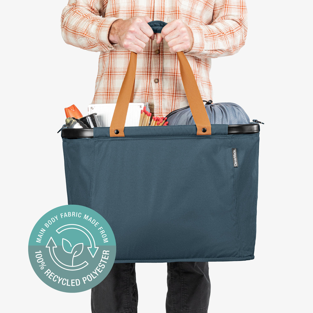 Person holding a blue tote bag with brown handles, featuring a recycling logo on a white background.