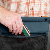 Person opening a blue fabric pouch with a plaid shirt in the background