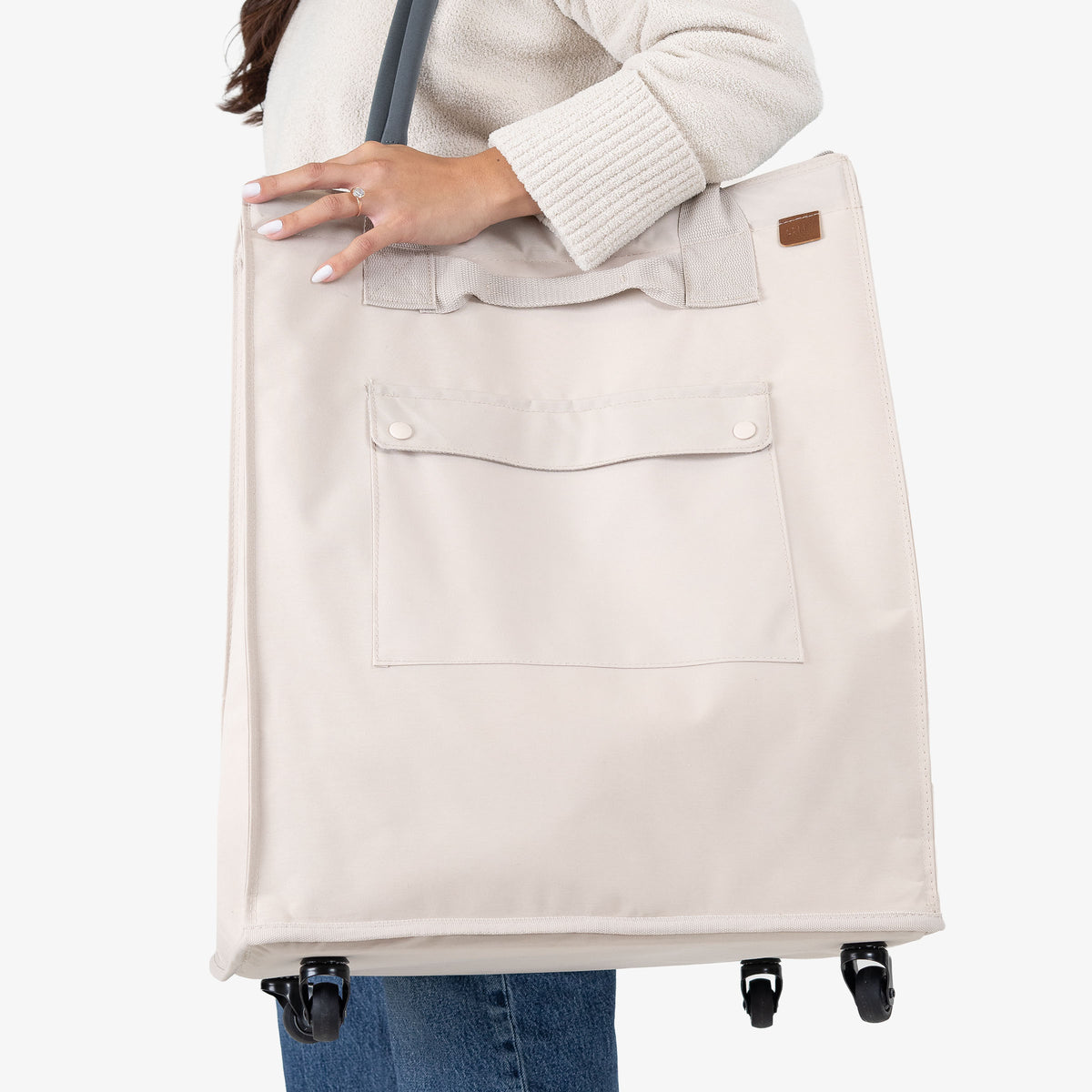Person holding a beige tote bag with wheels on a white background