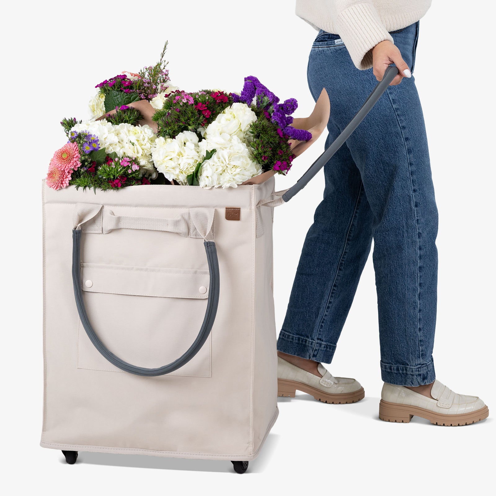Person pushing a cart with a large floral arrangement through a door.