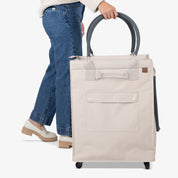 Person holding a beige rolling tote bag on a white background