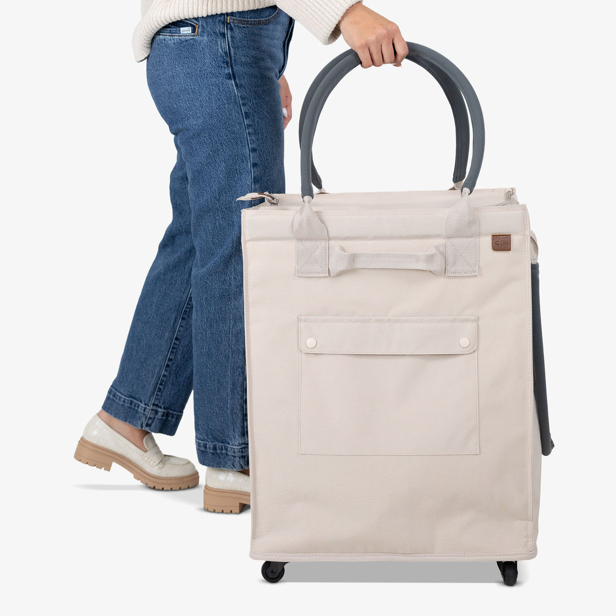 Person holding a beige rolling tote bag on a white background
