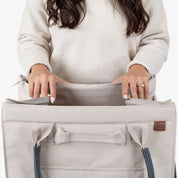 Person holding a beige tote bag with blue straps on a white background