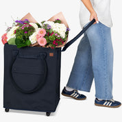 Person holding a navy blue rolling bag filled with flowers, with another person holding the handle.