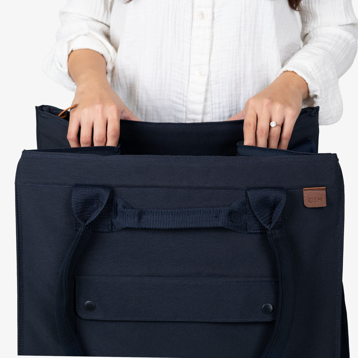 Navy blue bag with a brown leather patch held by a person wearing a white shirt.